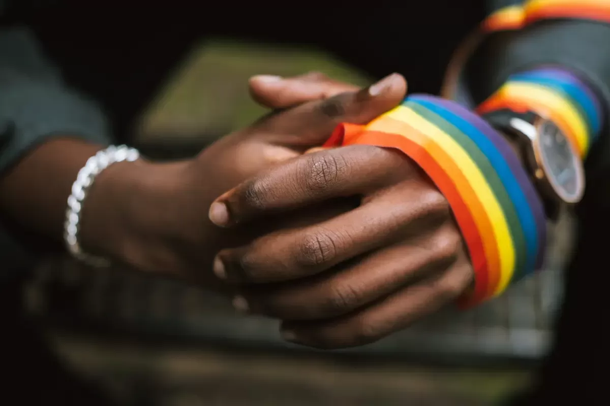 Two hands clasp together with a rainbow ribbon wrapped around them.